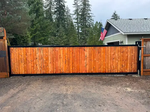 Finished cedar sliding driveway gate front view with US flag and home